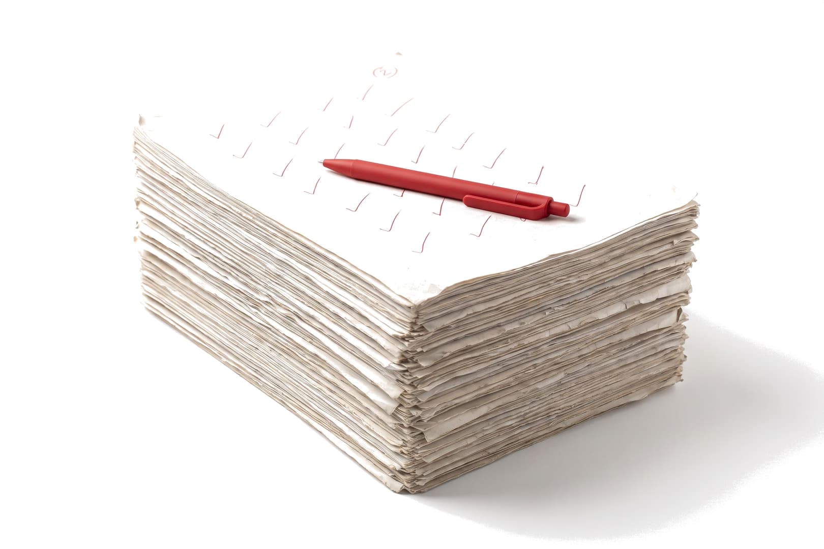 A tall squared stack of worked past papers, the top sheet covered in red ticks with a small circled total, a red ballpoint pen resting across it